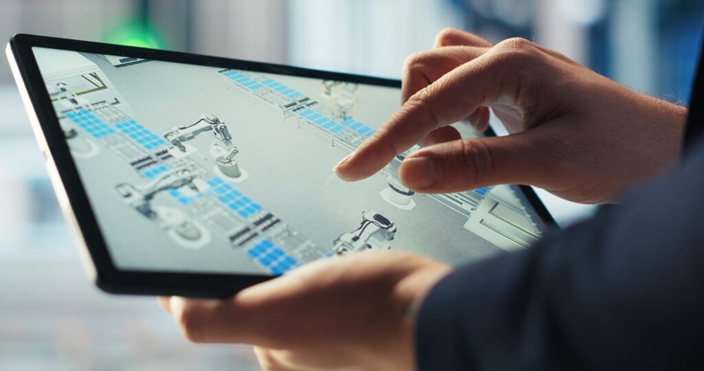 Technicien observant sur tablette un schéma de robots et de capteurs connectés en usine