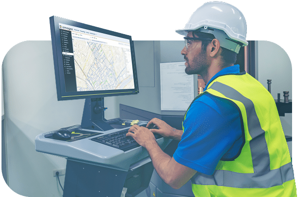 Un technicien en gilet de sécurité et casque blanc consulte l’application omogen sur un ordinateur de bureau affichant une carte de supervision des réseaux.