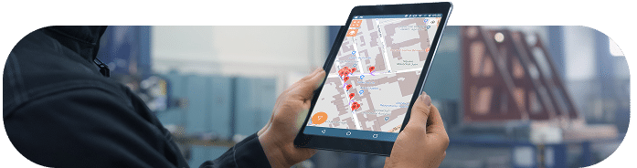 Un utilisateur tient une tablette affichant l’application Omogen GMAO avec une carte interactive et des points de repère, en environnement industriel.