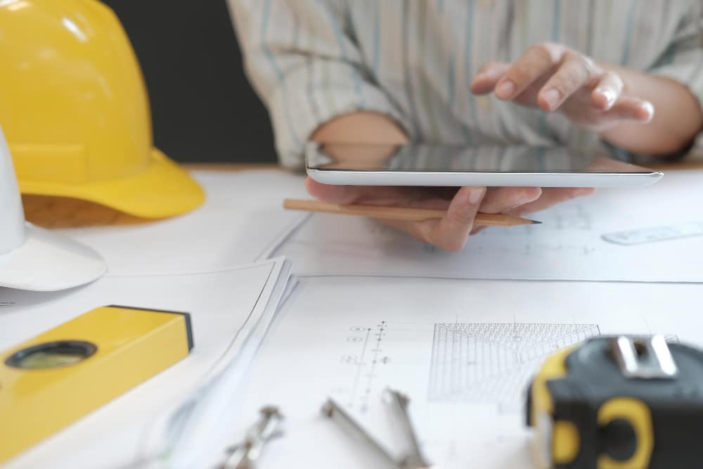 Technicien utilisant une tablette pour organiser le planning de maintenance préventive avec plans et outils de chantier