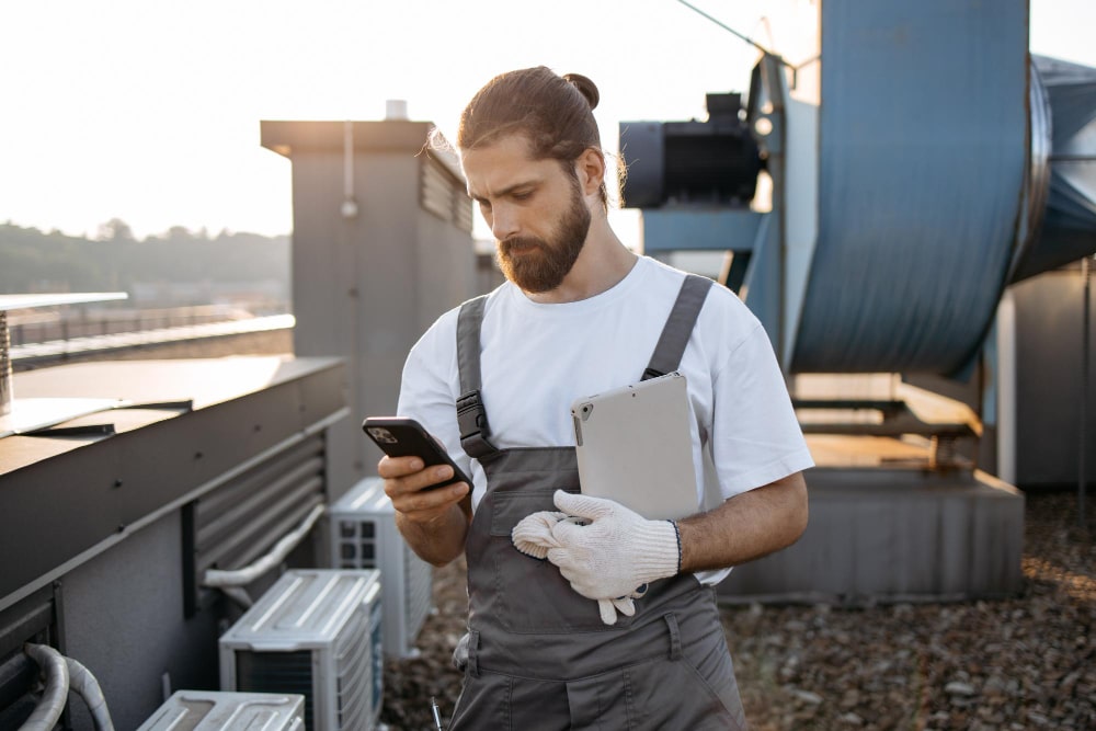 Technicien en maintenance sur un toit utilisant un smartphone et une tablette pour vérifier la connectivité.