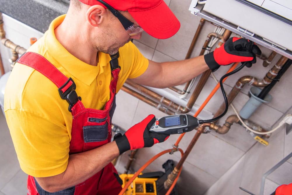 Technicien en manteau haute visibilité utilisant un détecteur de fuites acoustique sur un tuyau, casque sur les oreilles.