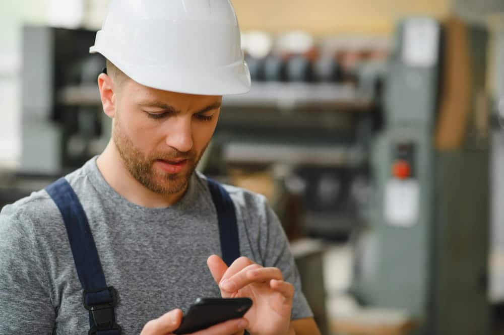 Technicien terrain utilisant une application mobile de gestion des interventions sur son smartphone en usine