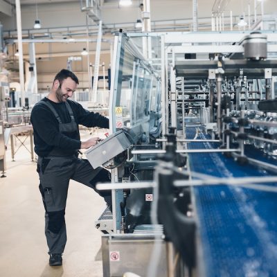 Happy smiled worker doing his job on Robotic factory line for processing and quality control of pure spring water bottled into canisters. Low light and small amount of noise visible.